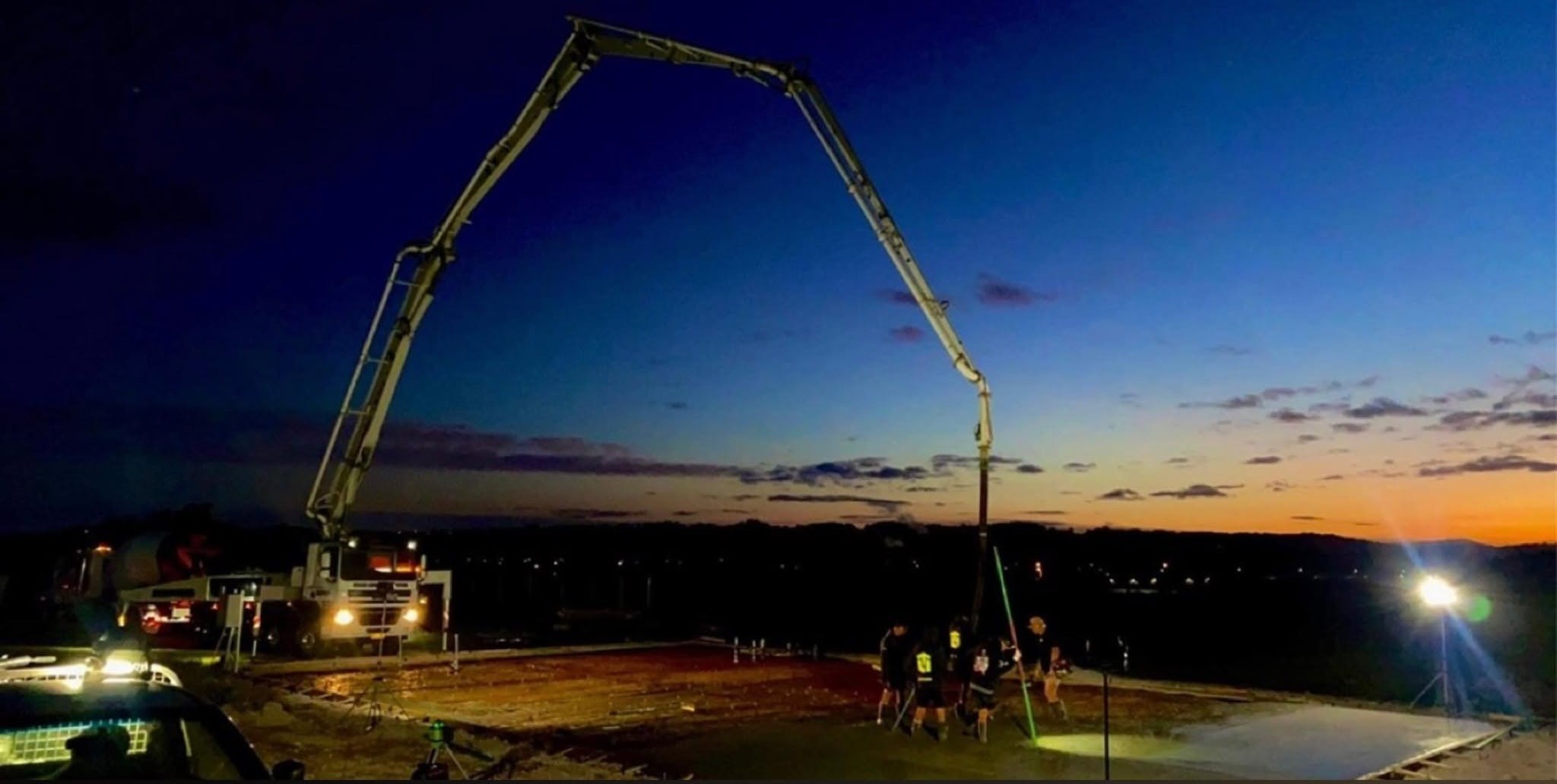 A concrete slab poured at dusk with a boom pump and work lights