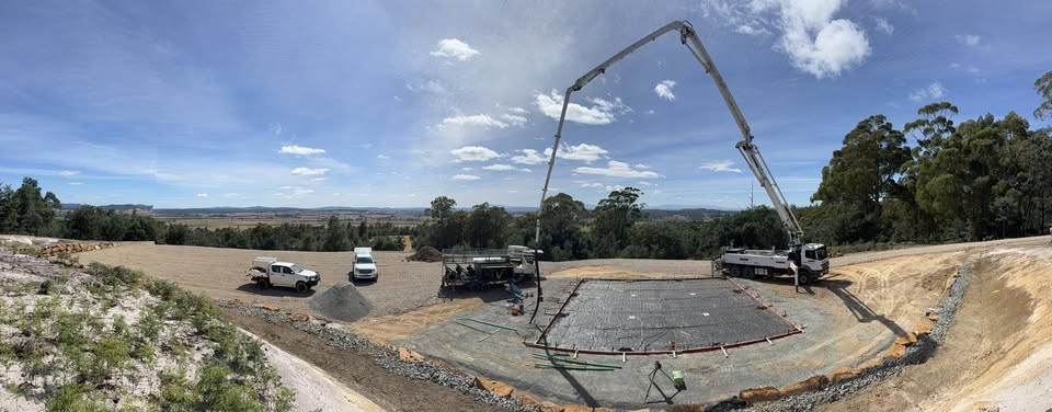 A large rural house slab being poured with a concrete boom pump on a clear day