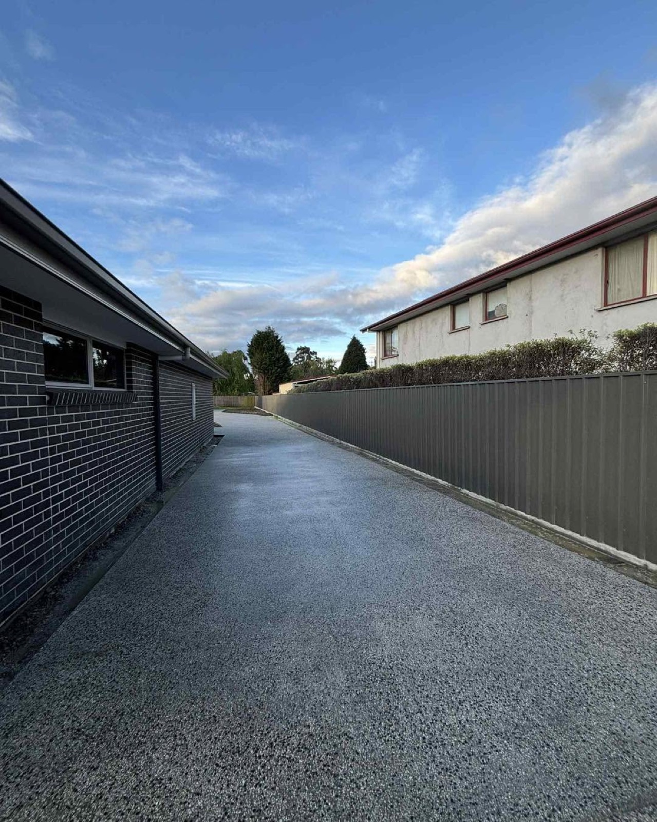 An exposed aggregate path running alongside a dark brick home