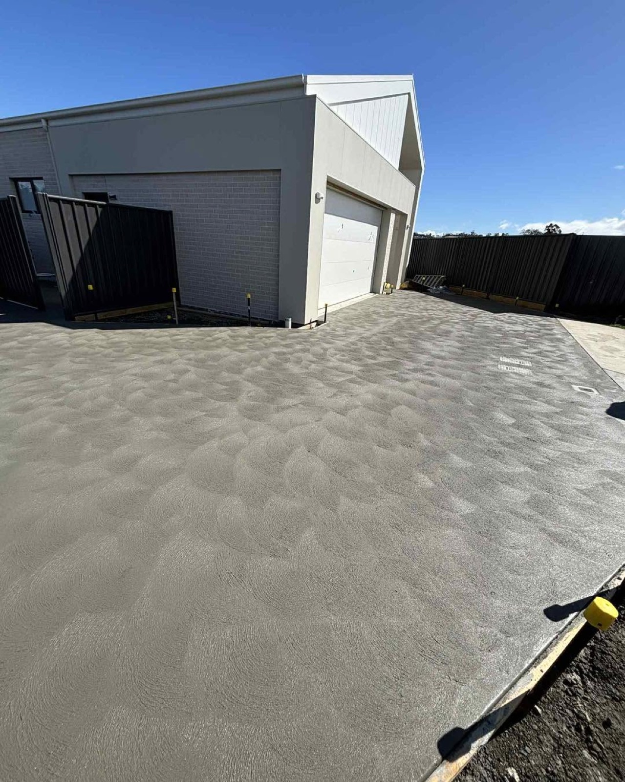 A fresh charcoal concrete driveway leading up to a white garage