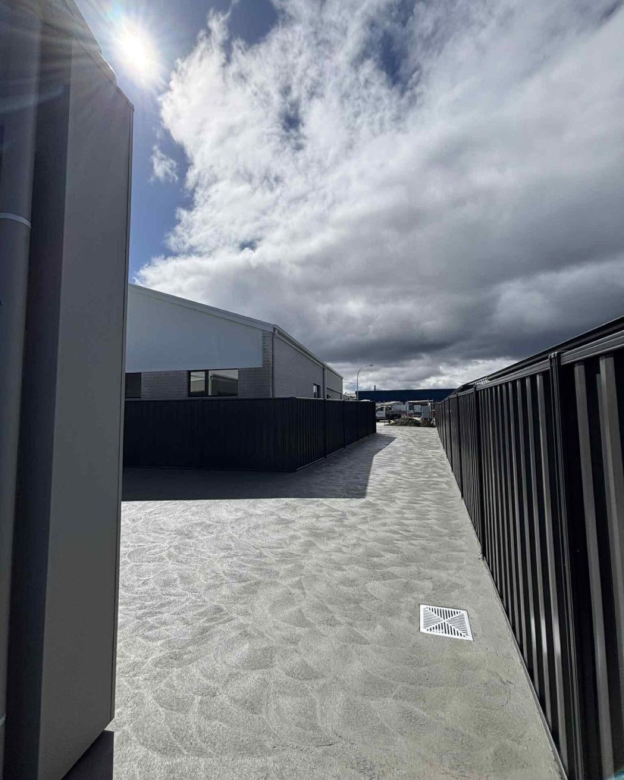 A charcoal concrete path running between a home and a colourbond fence