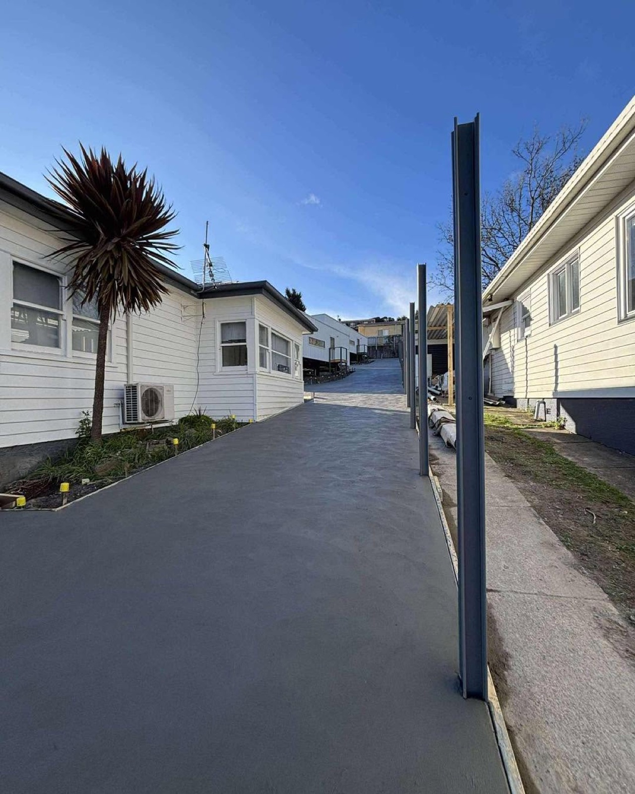 A charcoal driveway running between two homes past a palm tree